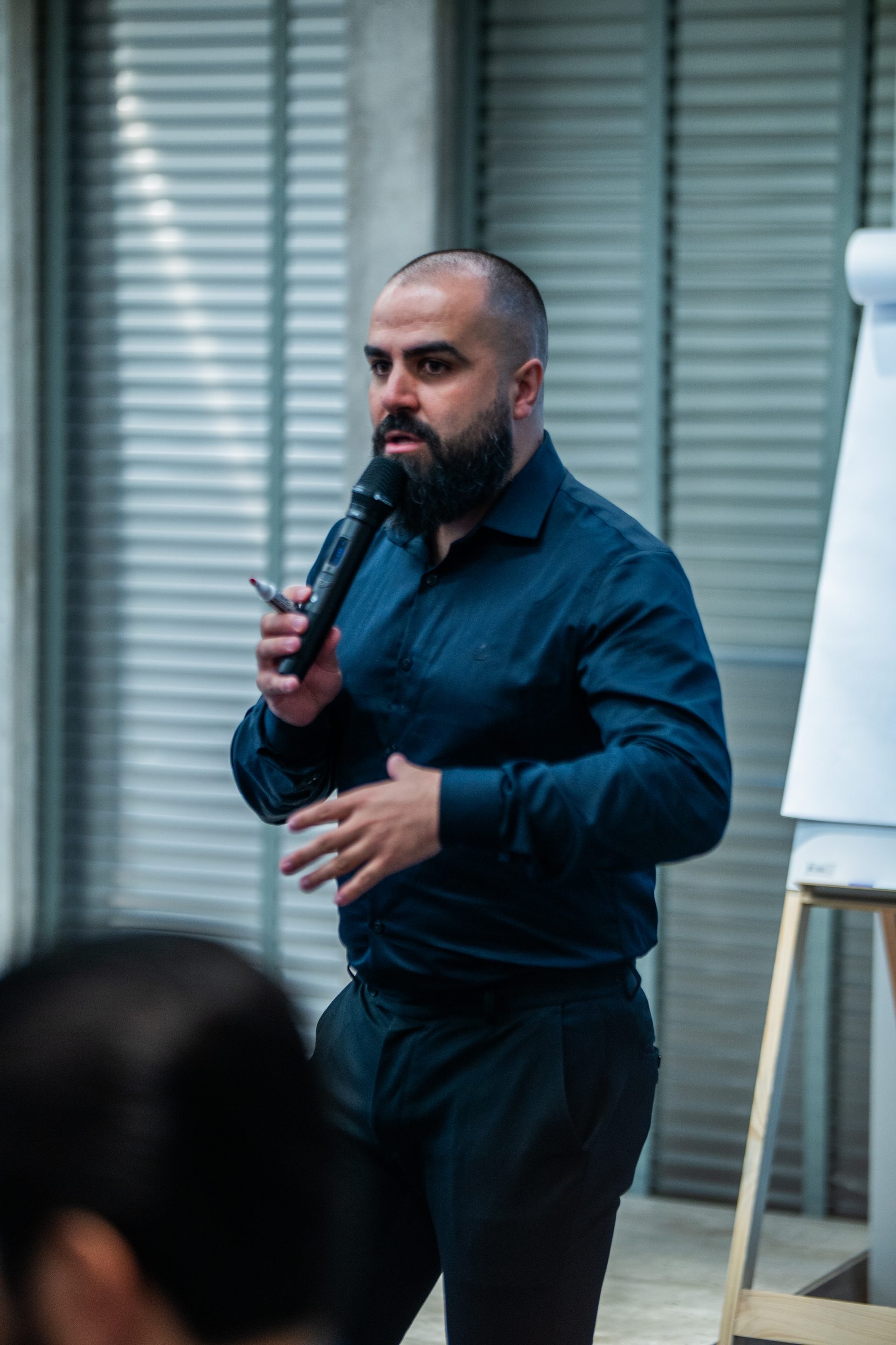 Rudnei Mazepa de camisa marinho falando ao microfone durante o evento DOMINA.IA